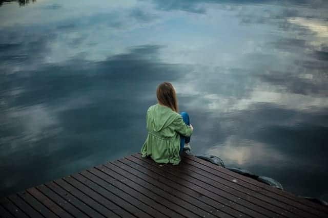  μια γυναίκα κάθεται στην άκρη μιας προβλήτας και κοιτάζει το νερό