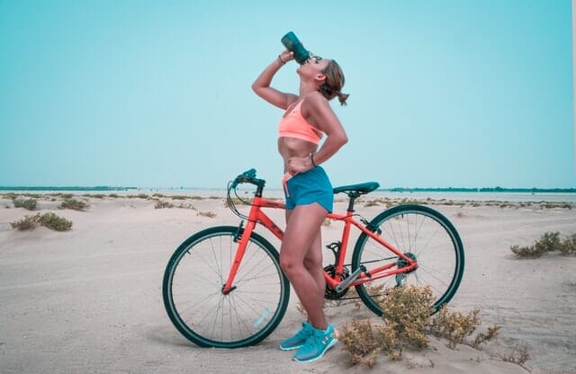  γυναίκα πίνει νερό από ένα μπουκάλι μετά από μια βόλτα με το ποδήλατο