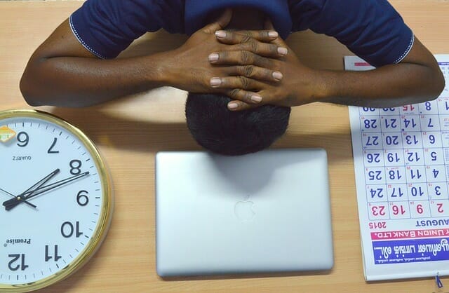  Ένας κουρασμένος άντρας κρατάει το κεφάλι του στο γραφείο του, δίπλα στο φορητό υπολογιστή του, το ημερολόγιο και το ρολόι του.