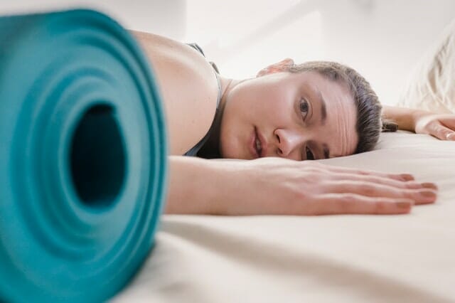  γυναίκα εξαντλημένη από την προπόνηση, δίπλα σε στρώμα γυμναστικής