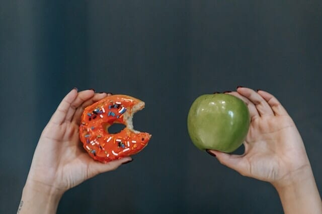  δύο χέρια, το ένα κρατάει ένα μήλο, το άλλο ένα ντόνατ