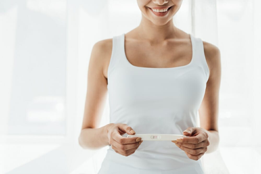  μια ικανοποιημένη γυναίκα κρατά ένα θετικό τεστ εγκυμοσύνης